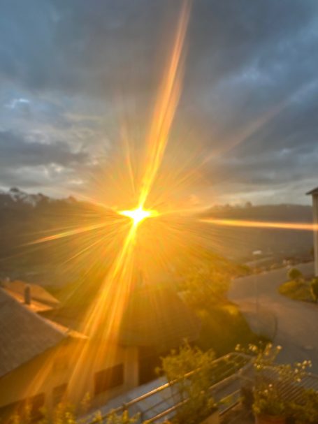 Sonnenuntergang mit strahlendem Licht über einer Landschaft und dunklen Wolken.